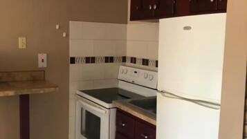 A kitchen with a stove, oven, and refrigerator, wooden cabinets, and a tiled backsplash.