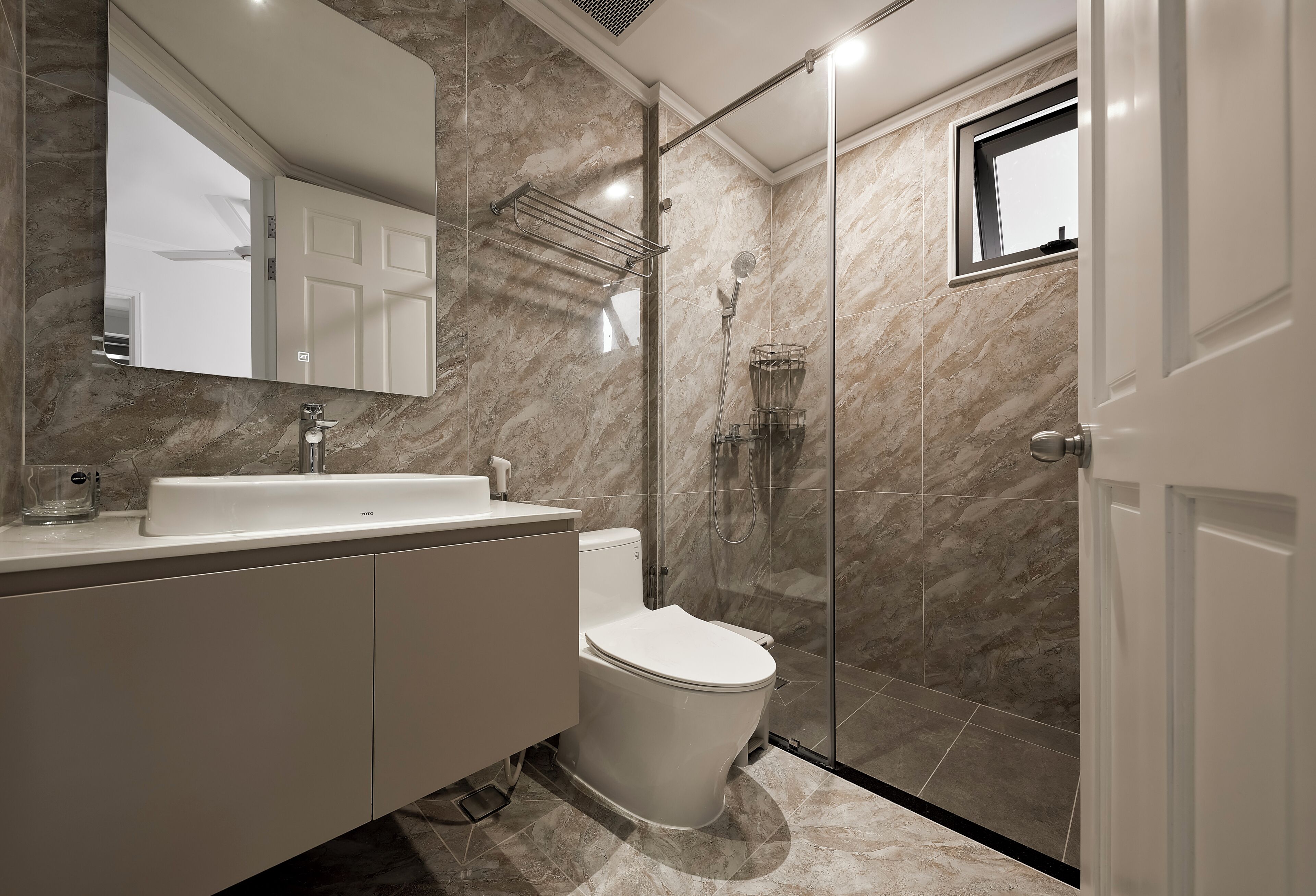 Une salle de bain moderne avec des toilettes blanches, une douche en verre et un mur recouvert de carreaux de marbre.