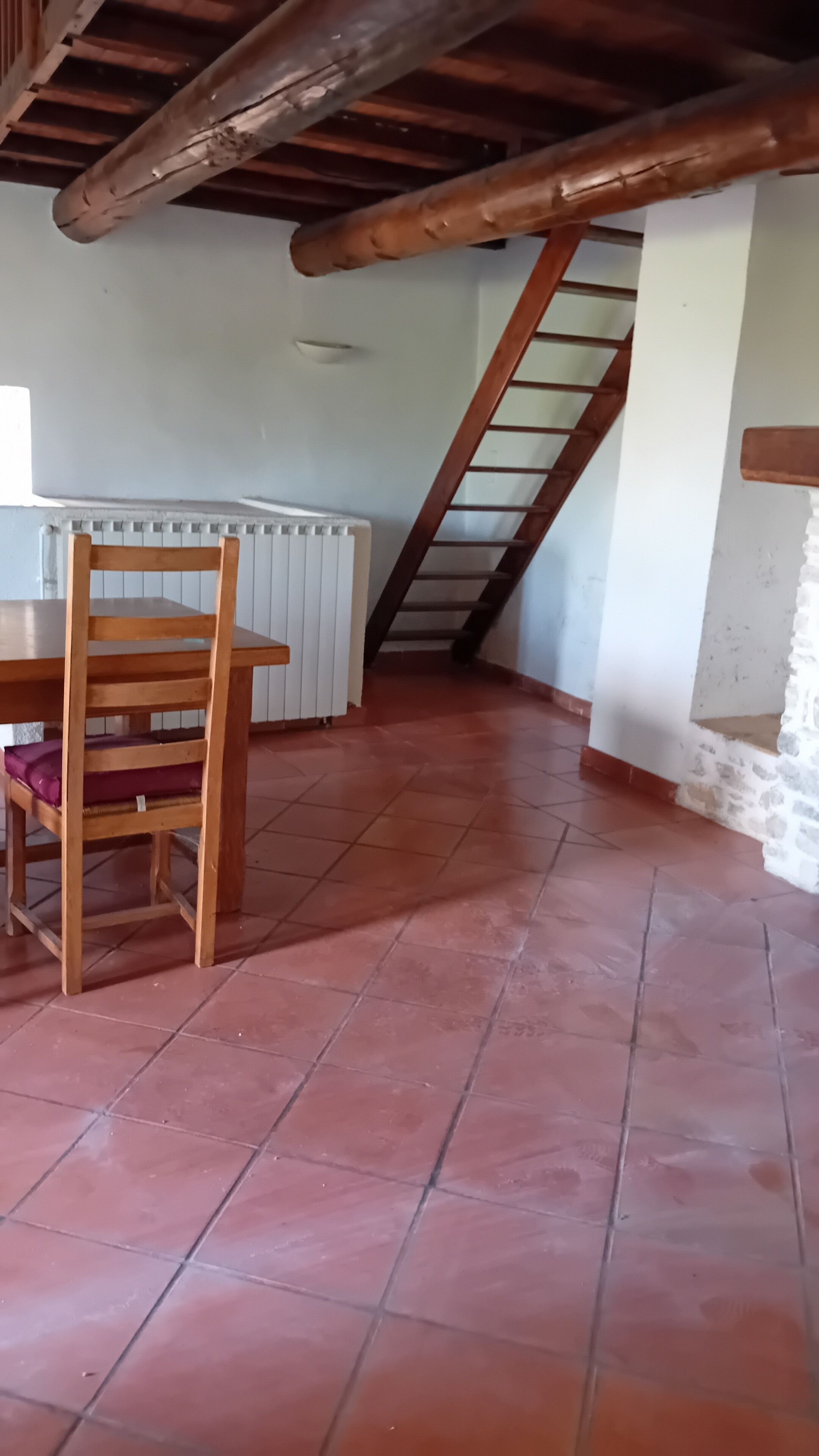 A room with a wooden table and chair, a radiator, a staircase, and a tiled floor.