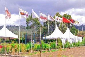 Une rangée de tentes blanches ornées de drapeaux, entourée de verdure et avec des collines en arrière-plan.