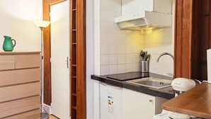 A compact kitchen with a wooden cabinet, a built-in oven, a sink, and a small refrigerator.
