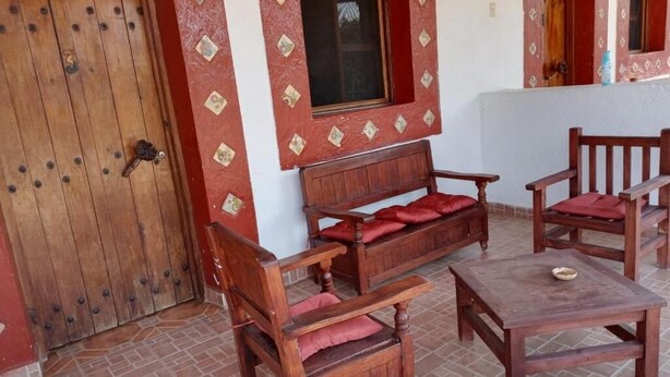 A wooden door with a window, a sofa with red cushions, and a small table. - Hotel Chalamu (Pátzcuaro)