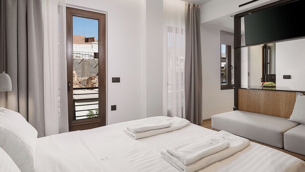 Habitación de hotel con cama, sofá, espejo y vistas al exterior.