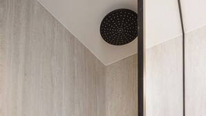Un baño moderno con pared de concreto, un accesorio de luz circular negro y un estante negro con artículos de aseo.