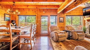 A cozy cabin interior with wooden walls, a dining area with wooden chairs, a sofa, and a television.