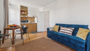A compact living space with a dining area, a blue sofa, and a kitchenette. - Charming 1BR in Le Marais - Bretagne (Paris)
