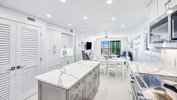 Una cocina moderna con armarios blancos, una isla grande y una zona de comedor con sillas blancas.