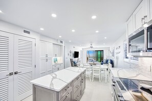 Une cuisine moderne avec des meubles blancs, un grand îlot central et un coin repas doté de chaises blanches.