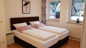 Una cama doble con ropa de cama blanca y rosa, un cabecero oscuro y un cuadro en la pared.