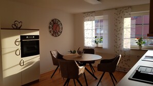 Una cocina moderna con horno empotrado, una mesa redonda con cuatro sillas, un reloj decorativo y una ventana con vistas a edificios.