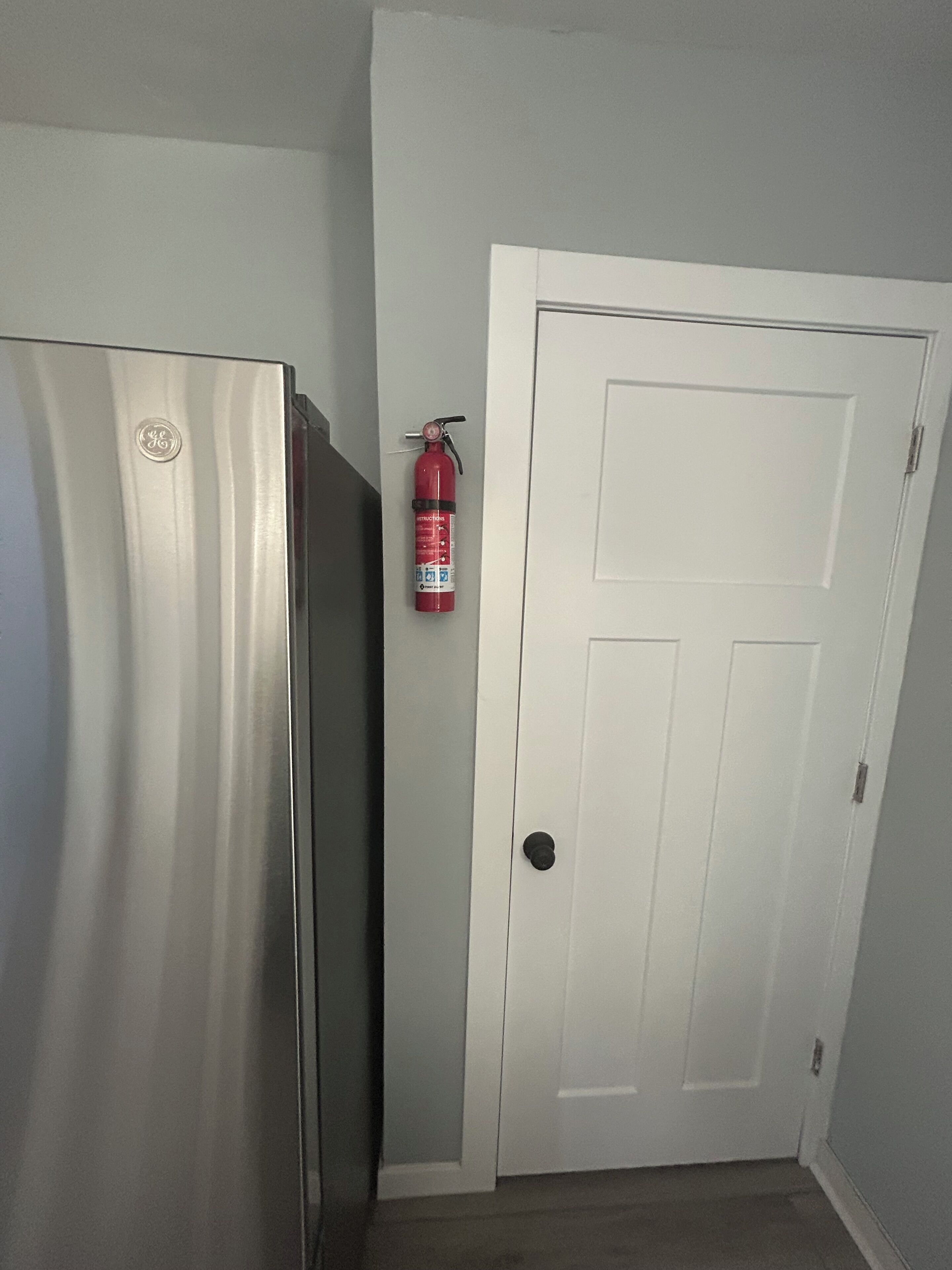 Eine Küche mit einem Edelstahl-Kühlschrank, einer weißen Tür und einem roten Feuerlöscher, der an der Wand befestigt ist.