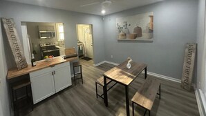 Una cocina compacta con armarios blancos, un microondas y una estufa. Hay una mesa de madera con bancos y un ventilador de techo.