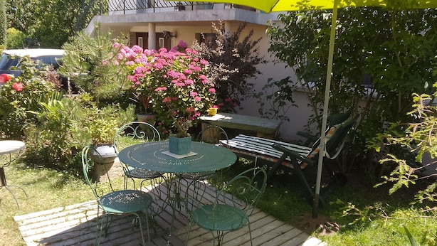 Un espace patio avec une table ronde et des chaises, entouré de plantes en pot et agrémenté d’un parasol jaune.