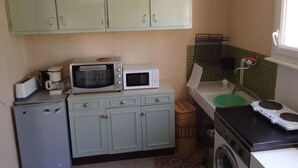 Une cuisine compacte équipée de deux fours encastrés, d’un petit réfrigérateur, d’un lave-linge et d’un évier avec une cuve verte.