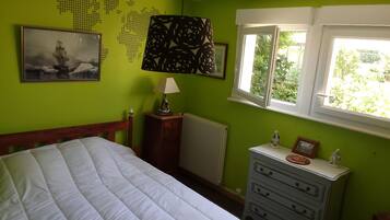 Een slaapkamer met een bed, een dressoir, een wereldkaart aan de muur, een lamp en een raam met uitzicht op groen.