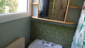 Une salle de bain avec un lavabo blanc, une fenêtre et des carreaux verts à motifs.