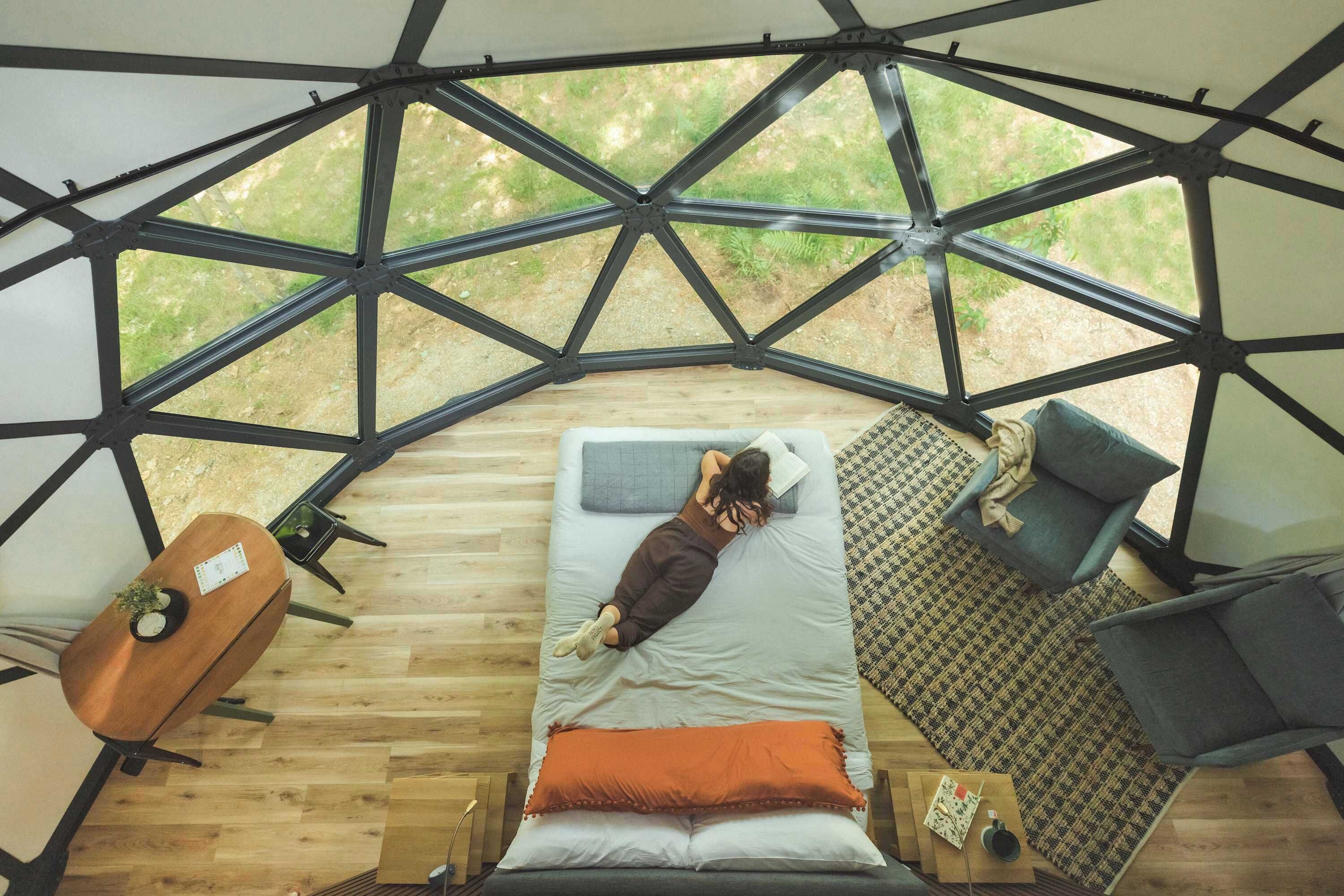 A geodesic dome structure with a bed, a chair, and a table inside.