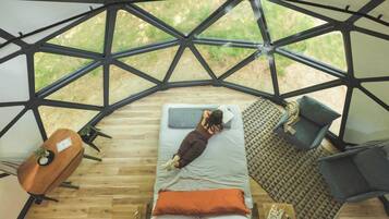 A geodesic dome structure with a bed, a chair, and a table inside.