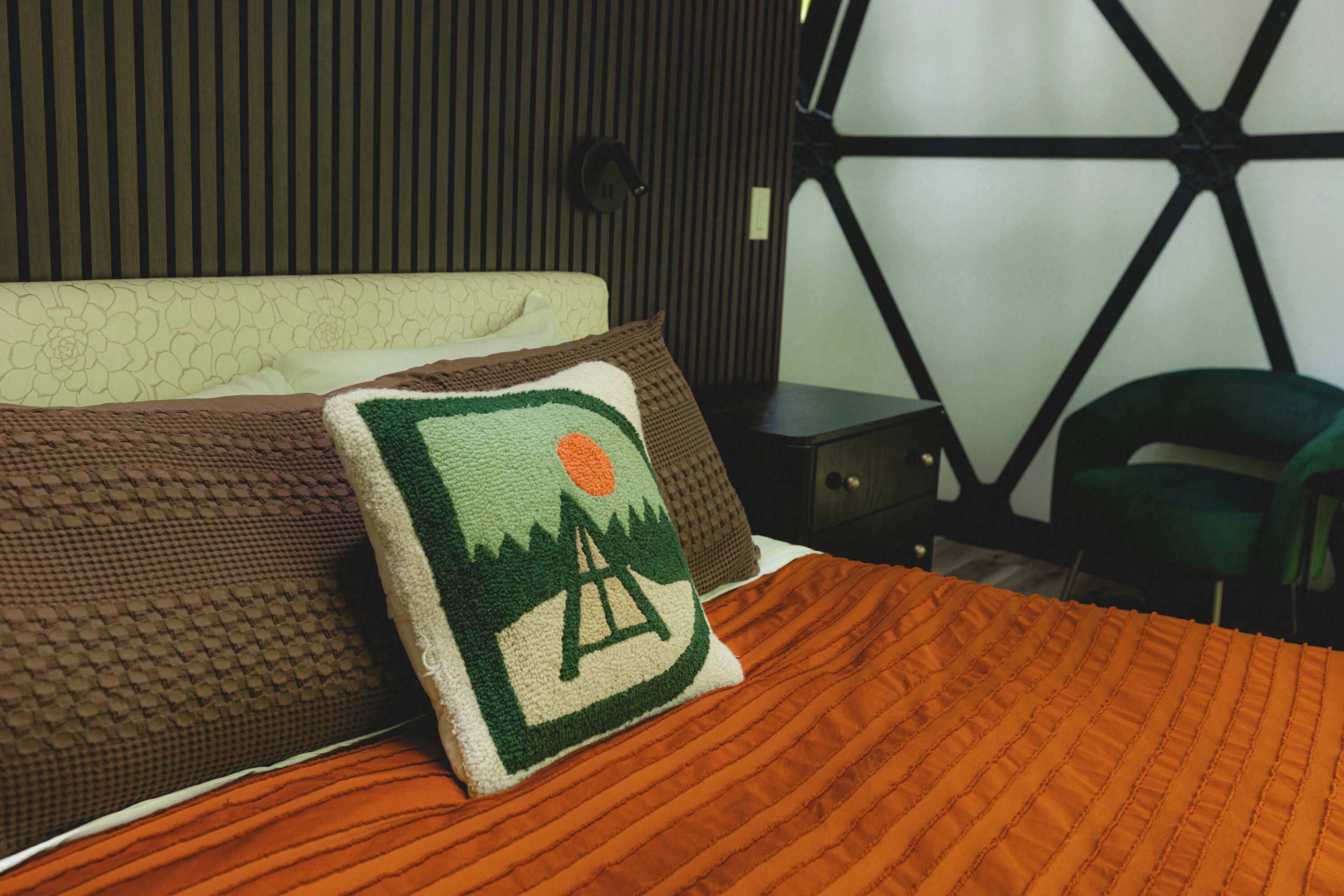 A bed with a patterned blanket, pillows, and a quilt with a landscape design.