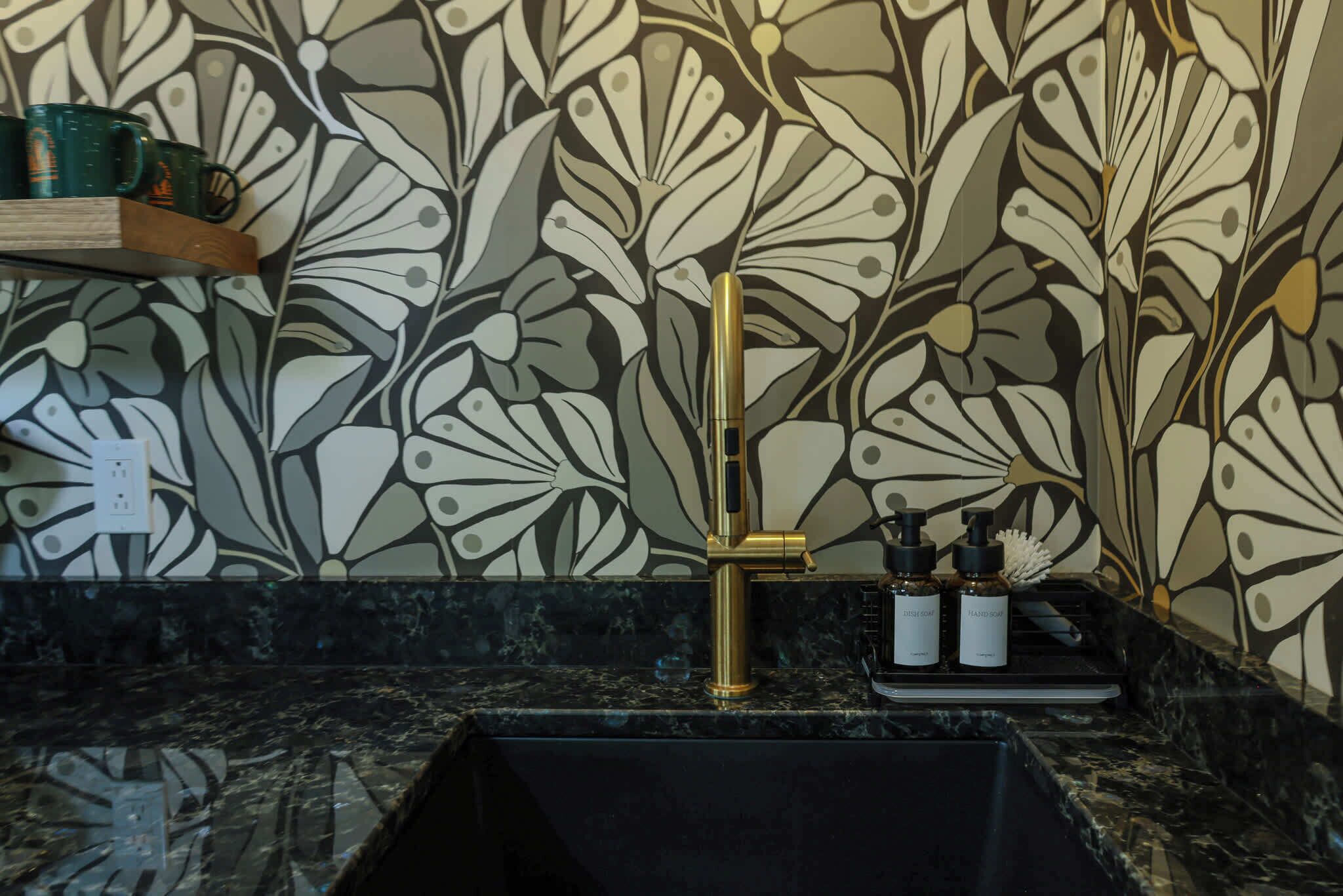 Een badkamer met een zwarte wastafel, een gouden kraan en een behang met bloemenmotief.