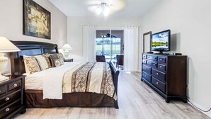 Un dormitorio con cama, cómoda, televisor y vistas al exterior.