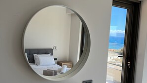 Un dormitorio con un espejo redondo, una cama, una mesita de noche y vistas al exterior a través de una ventana.