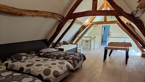Une chambre confortable située dans les combles, avec des poutres apparentes, un lit recouvert d’une literie à motifs et une table de baby-foot.