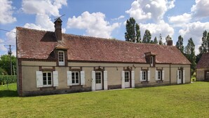 Un long bâtiment d’un seul étage, doté d’un toit en tuiles et de volets blancs, entouré d’une pelouse verdoyante.
