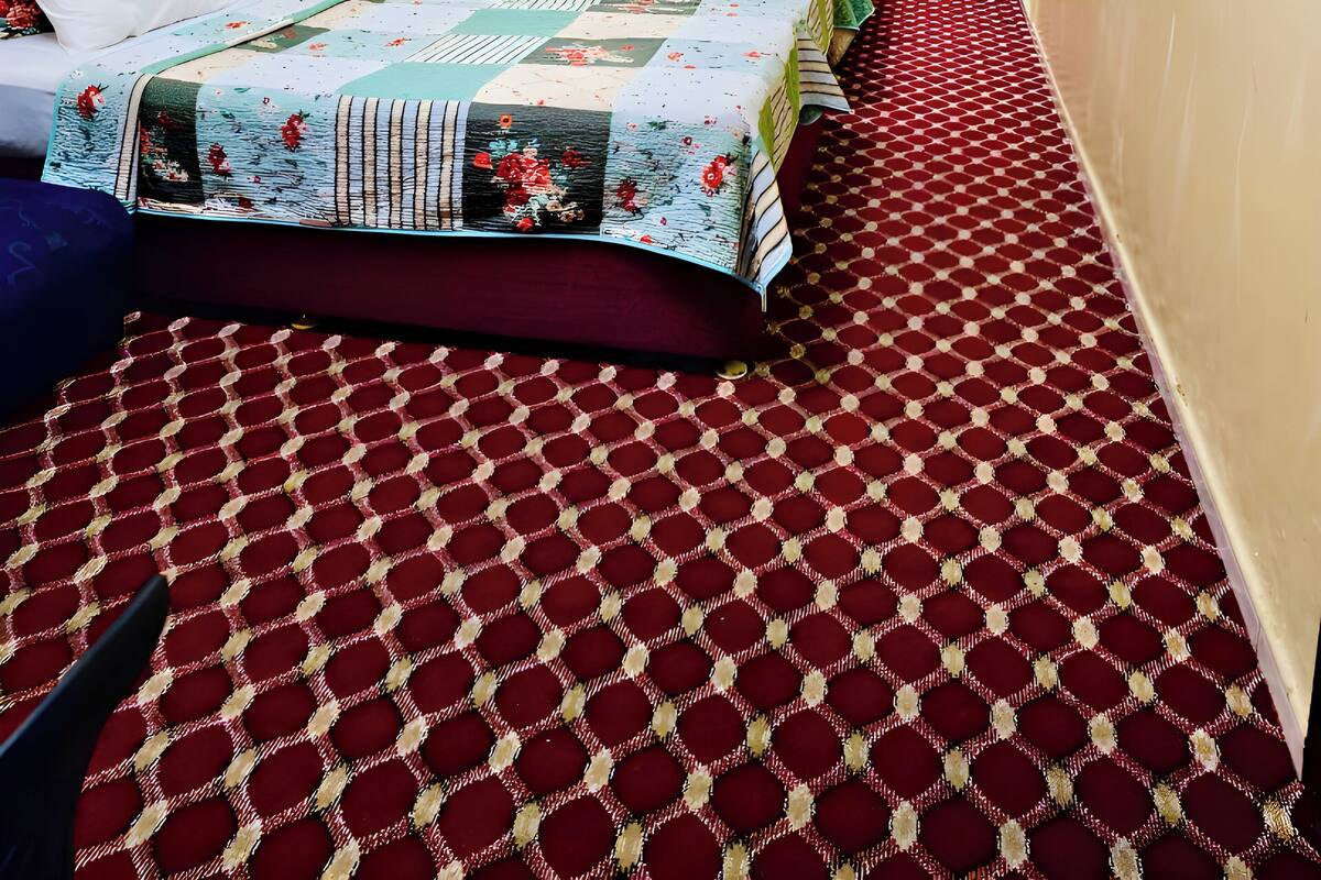 A hotel room with a wooden headboard, a bed with a floral quilt, a red patterned carpet, a ceiling fan, and a door.