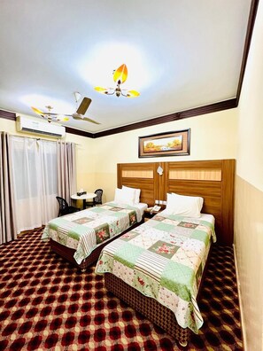 A hotel room with two beds, a ceiling fan, an air conditioning unit, a framed picture on the wall, and a patterned carpet. - AL AHRAR HOTEL (Dubai)