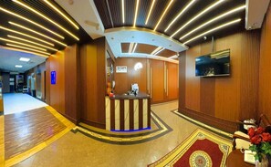 A hotel reception area with a reception desk, a flat-screen TV, and a patterned carpet. - AL AHRAR HOTEL (Dubai)