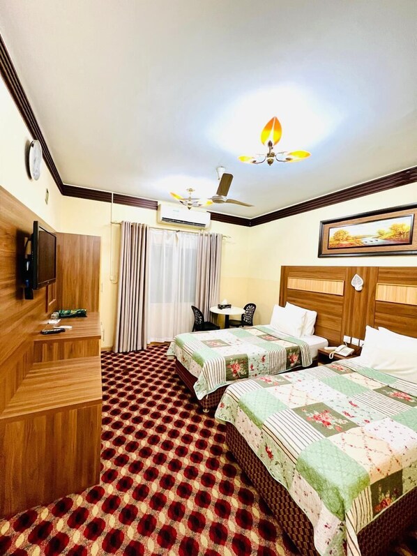 A hotel room with two beds, a wooden desk, a television, and a ceiling fan. - AL AHRAR HOTEL (Dubai)