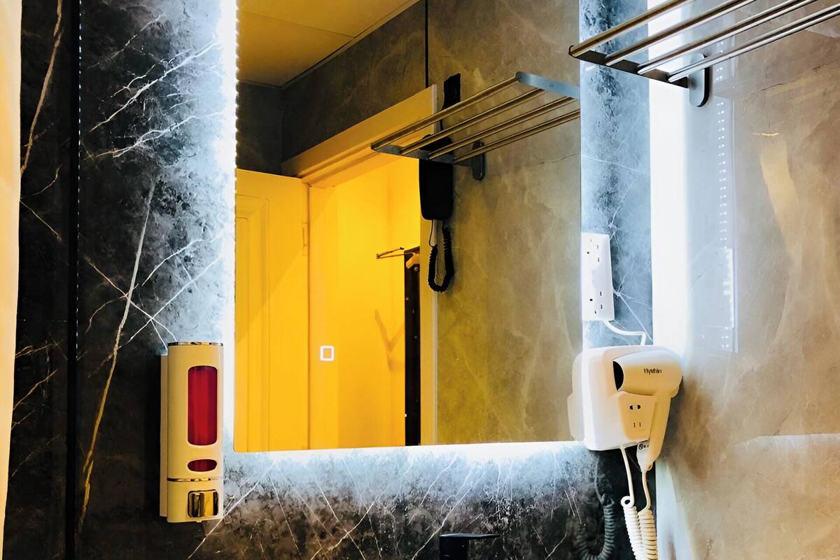 A modern bathroom with a marble wall, a large mirror, a white sink, and a handheld hair dryer mounted on the wall.