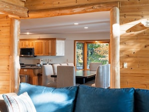 Un interior moderno con pared de madera, una zona de comedor con sillas, un sofá y una cocina con armarios y televisor.