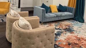 Ein Wohnzimmer mit Sofa, Sesseln, einem gemusterten Teppich, einer Treppe und einer Tür mit Spiegel.