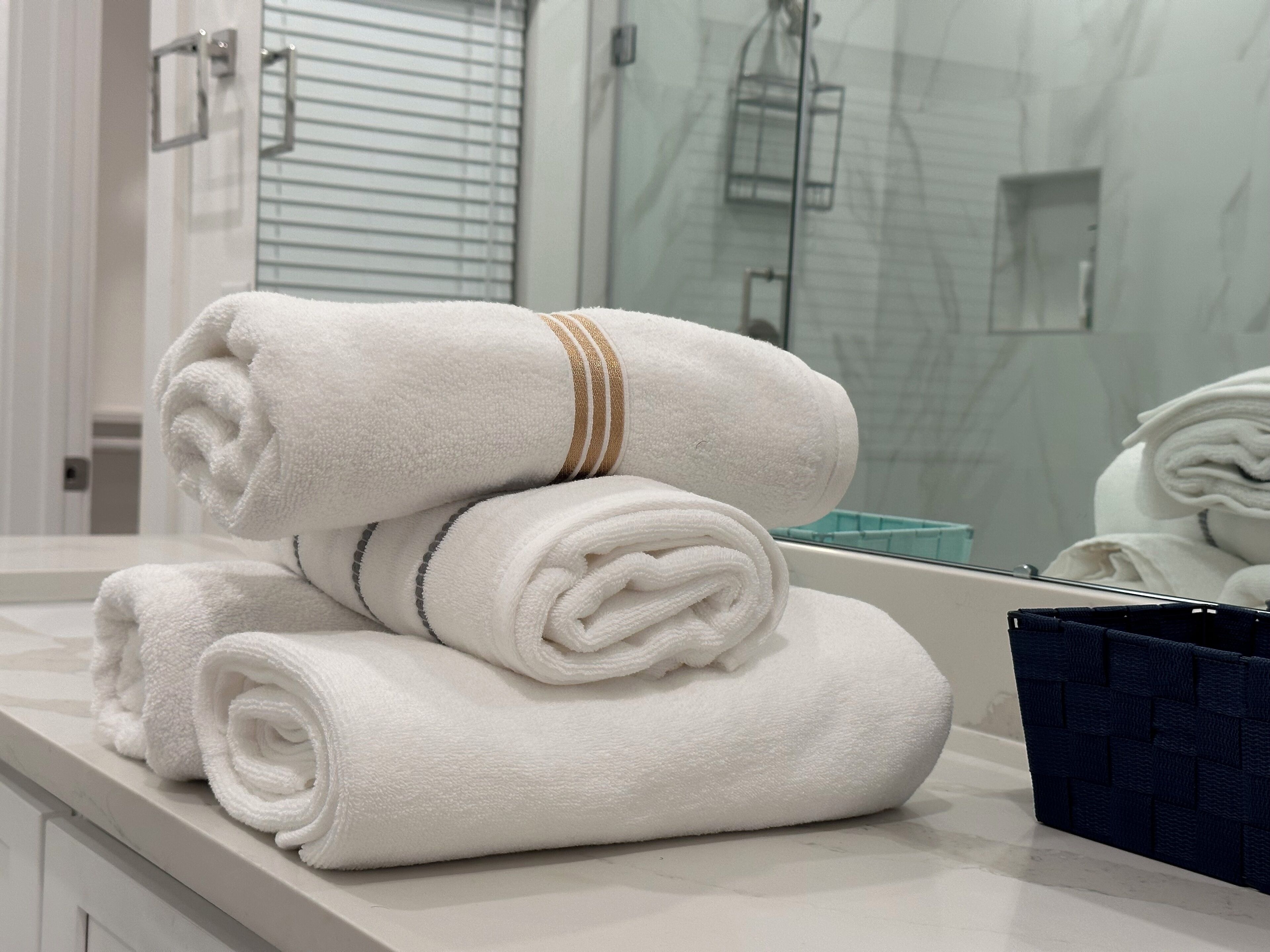 Un baño con toallas blancas apiladas sobre un mostrador y una cesta azul.