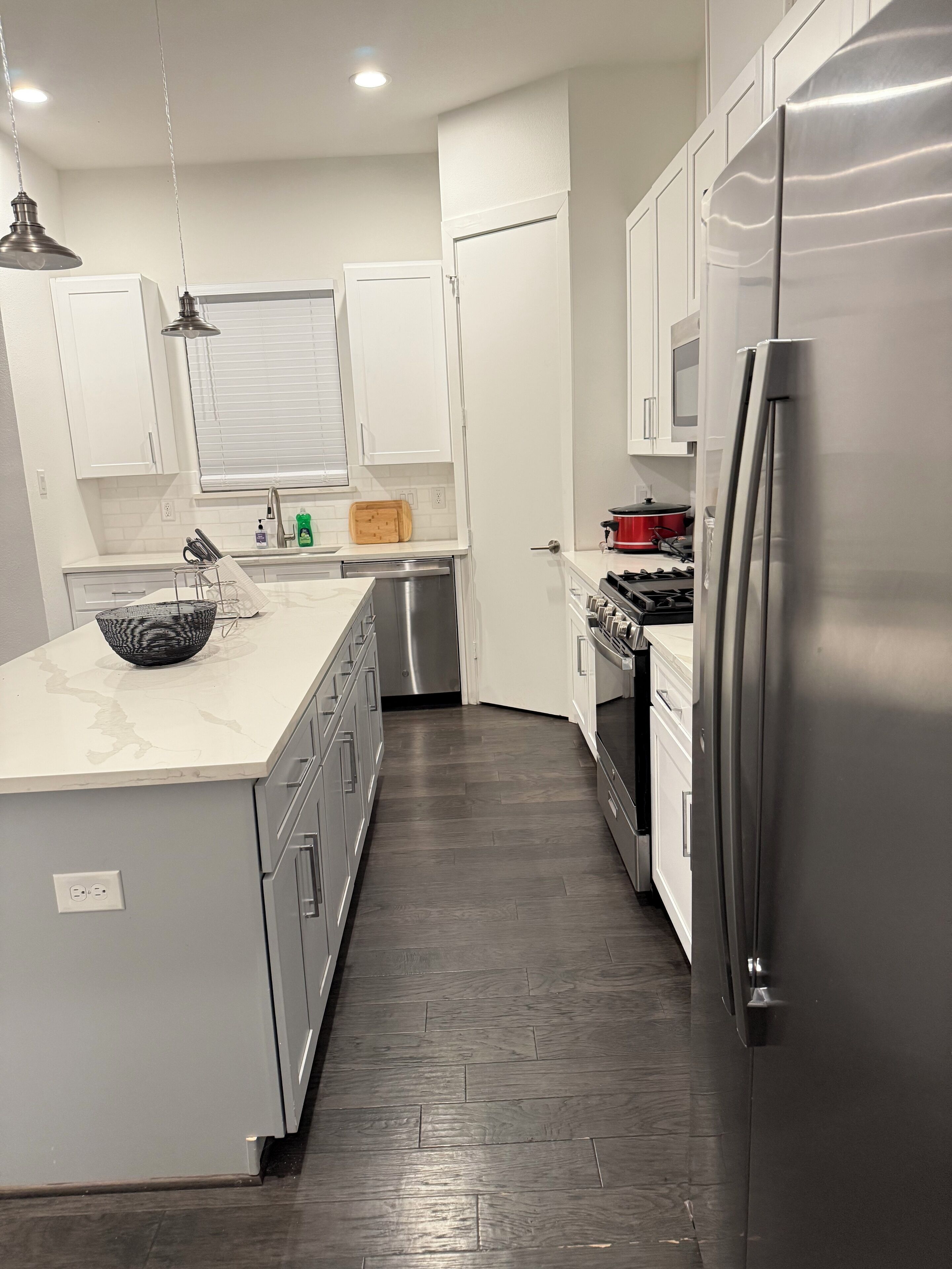 Una cocina moderna con gabinetes blancos, un refrigerador de acero inoxidable, un horno empotrado y un microondas.
