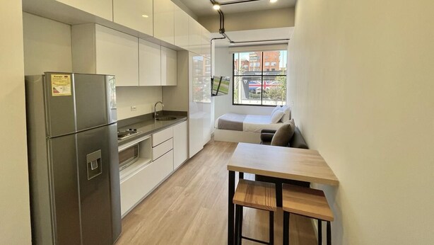 Una cocina moderna con electrodomésticos de acero inoxidable, una mesa de comedor de madera y vistas a la ciudad a través de amplios ventanales.