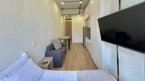 Habitación de hotel compacta con cama, sofá, una mesita, televisor y kitchenette.