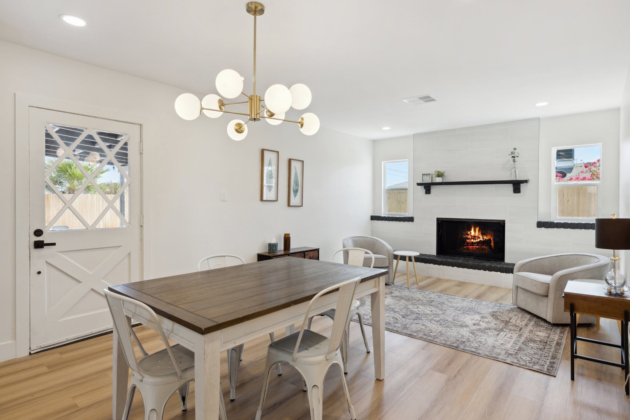 Een moderne woonkamer met een open haard, een eetgedeelte met een houten tafel en witte stoelen, en een plafondlamp.