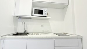 Et moderne køkken med hvide skabe, indbygget mikroovn, stålvask og en glas skål på bordet.