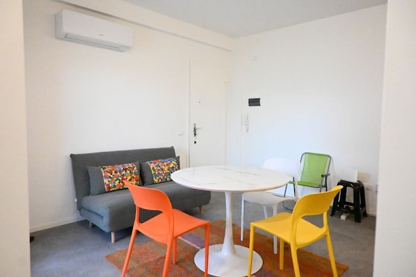 A small room with a gray sofa, colorful pillows, a white table, and two chairs.