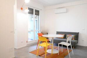 A room with a white table, two chairs, a gray sofa, and a window with a view. - SE193 – Senigallia, brand-new studio with air conditioning (Senigallia)