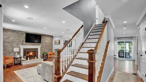 Un salón espacioso con chimenea, una escalera y un televisor grande montado en la pared.