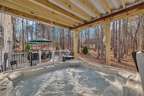 Area idromassaggio con una terrazza in legno, arredi da esterno e vista su una zona boschiva.
