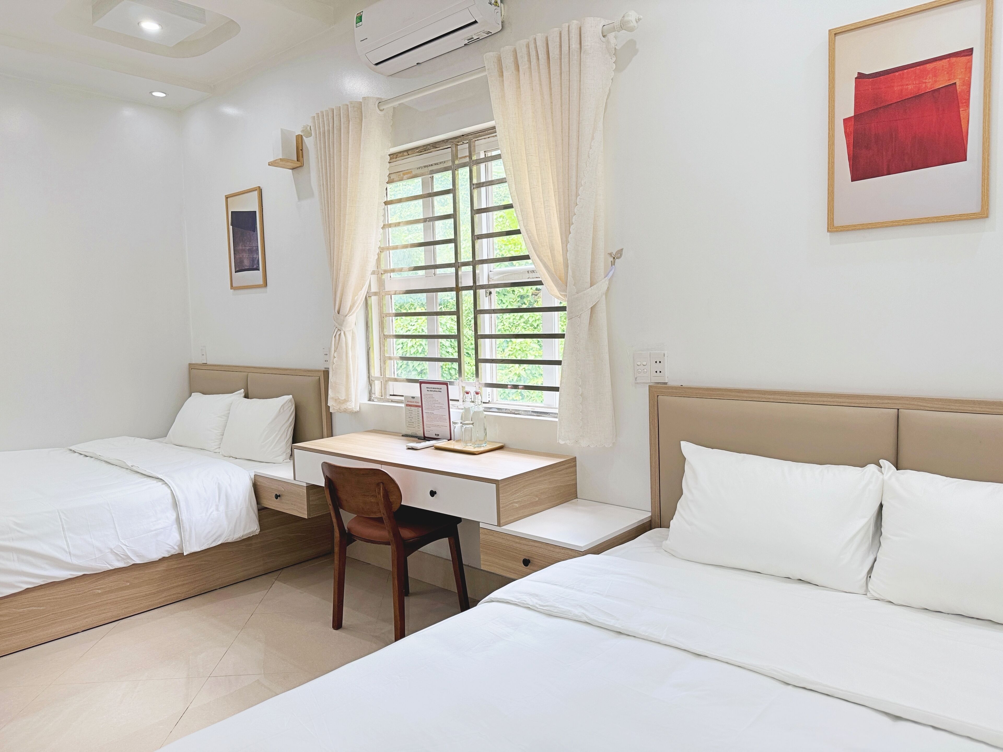 A hotel room with two beds, a desk, a chair, and a window with curtains.