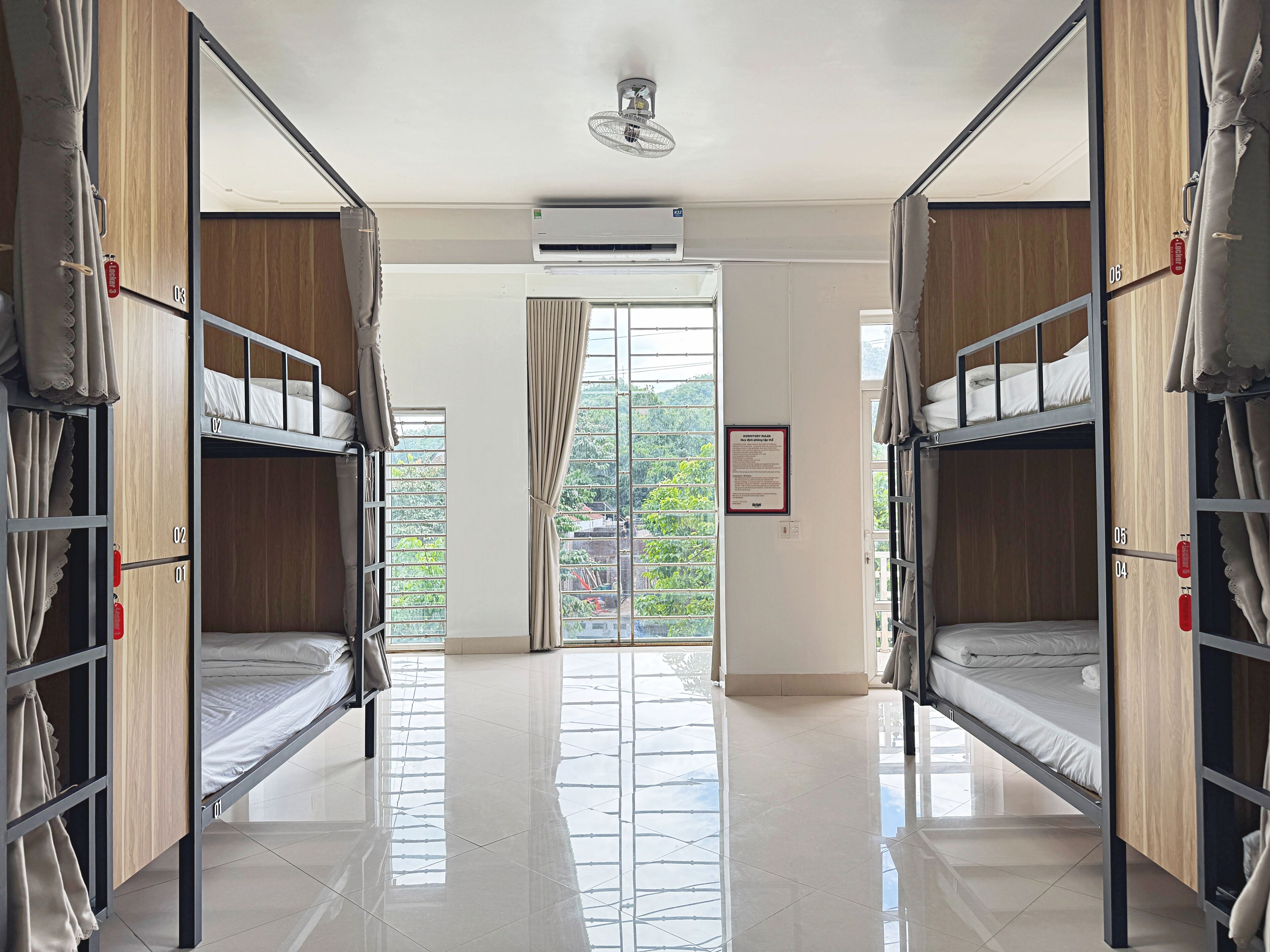 Une chambre d’hôtel avec des lits superposés, un sol carrelé, un appareil de climatisation et une vue sur la verdure.