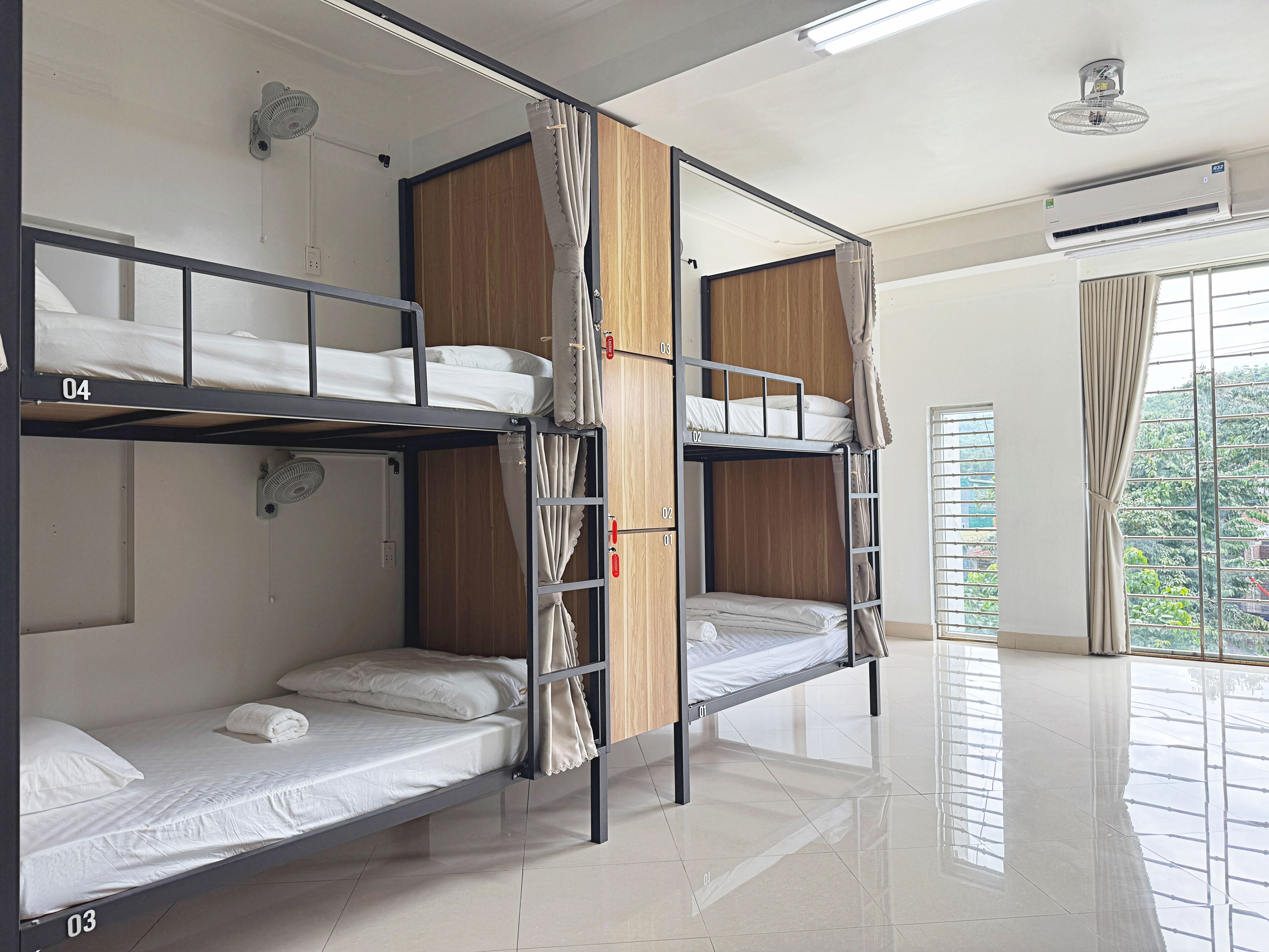 Un dormitorio con literas de tres niveles, cada una con colchón y almohadas, un armario de madera y un ventilador de techo.