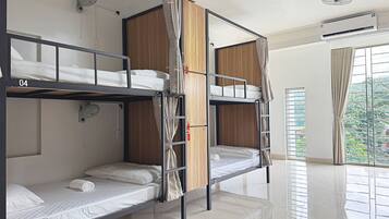 Un dormitorio con literas de tres niveles, cada una con colchón y almohadas, un armario de madera y un ventilador de techo.