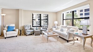 A living room with a beige sofa, a patterned armchair, a coffee table, and a floor lamp. - Gulf and Bay Club - 410 - 3 Pools! (Siesta Key)
